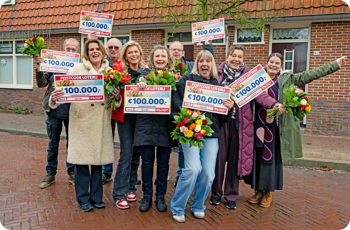 Een groep winnaars staat juichend in een straat met rijtjeshuizen, met in hun handen cheques van €100.000 en bloemen.