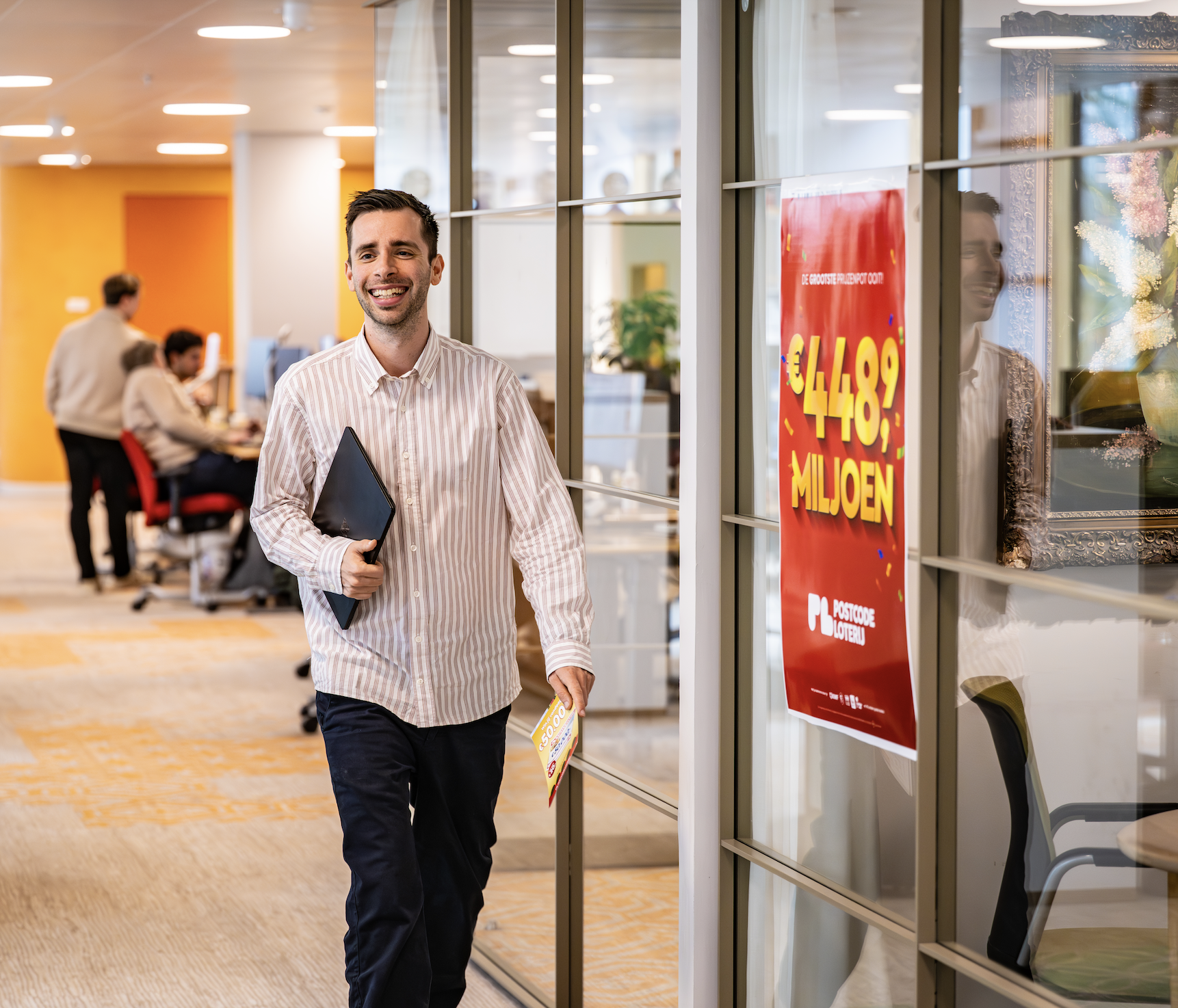Koen Coopmans loopt over de Marketingafdeling van de Postcode Loterij. Op een raam hangt een rode poster.
