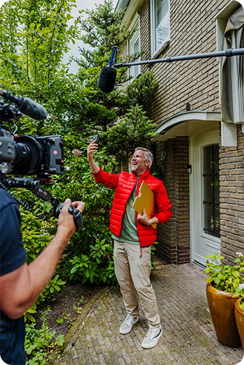 Ambassadeur Winston Gerschtanowitz staat beeldbellend voor de deur van een winnaar. De camera en de microfoon zijn zichtbaar.